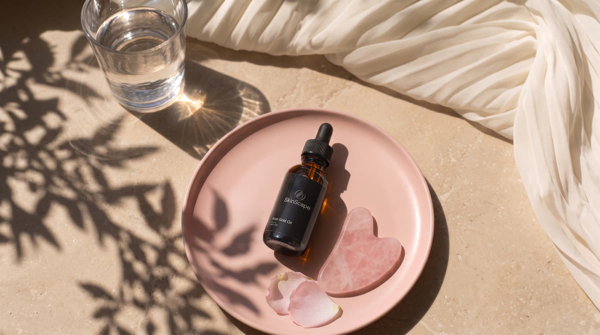 Rose gold facial oil beside a pink gua sha on a plate